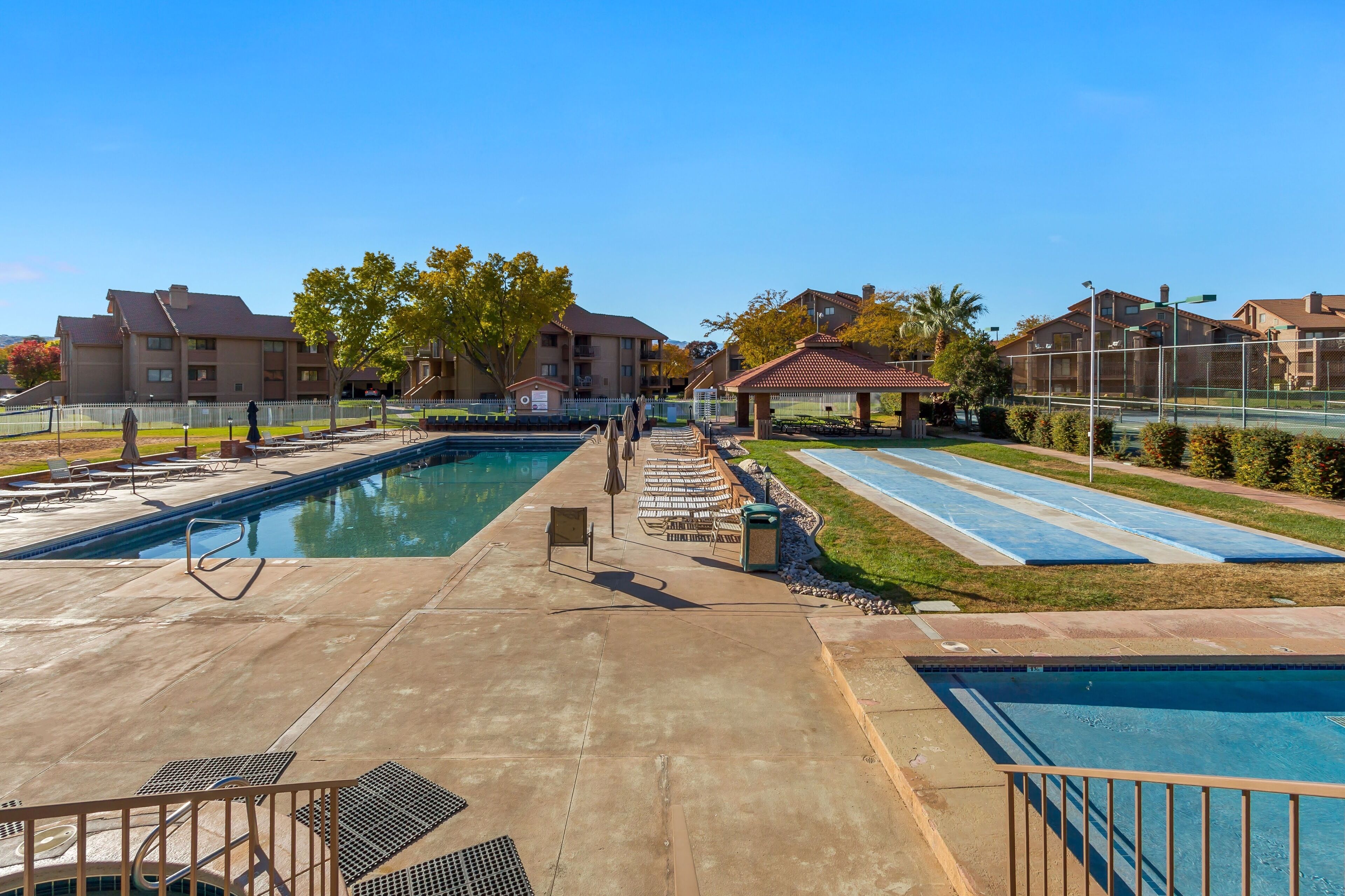 A swimming pool area with two pools, lounge chairs, and a gazebo.