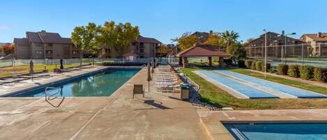 A swimming pool area with two pools, lounge chairs, and a gazebo.