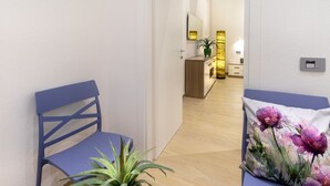 Moderni hotellihuone, jossa on puulattia, sininen tuoli, pieni ruukkukasvi ja koristeellinen, kukkakuviollinen tyyny.