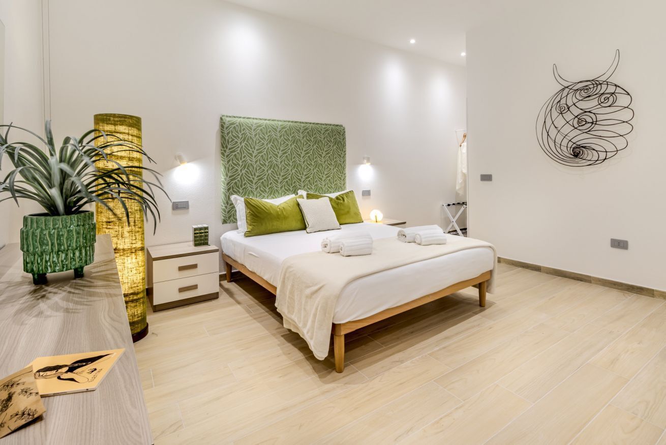 Ein modernes Schlafzimmer mit einem Bett, Nachttischen, einem Kopfende mit grünem Muster, einem Wandbild und einer Topfpflanze.