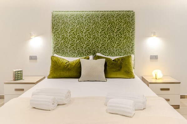 A neatly made bed with green and white pillows, two bedside lamps, and two rolled towels on the bed. - Artis Rooms - Suite Green (Cagliari)