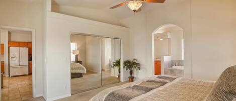 Un dormitorio con una cama grande, ventilador de techo, espejo y puerta corrediza que da a un baño.