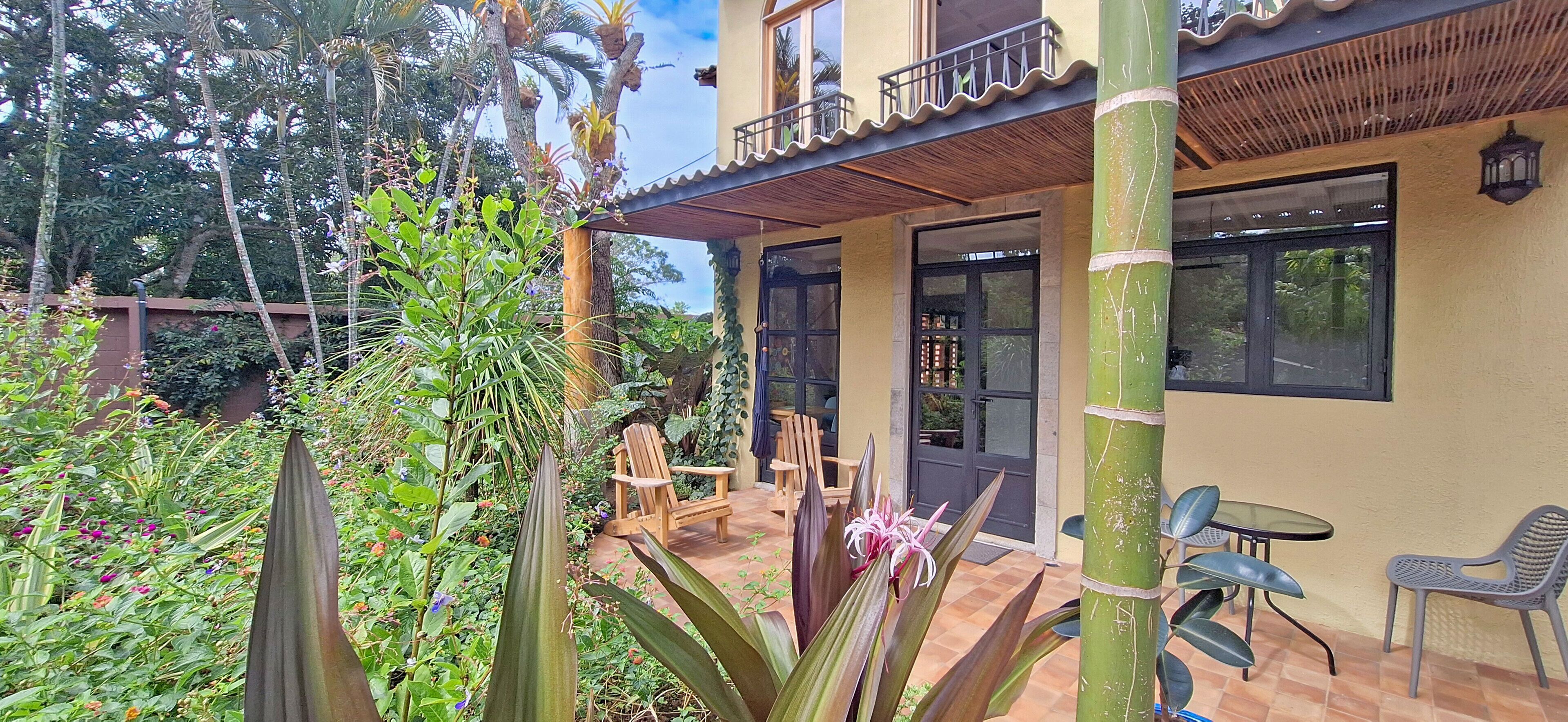 A two-story building with a balcony, outdoor seating, and lush greenery.