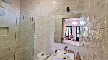 Une salle de bain avec une douche à parois de verre, un lavabo avec un miroir et des toilettes.