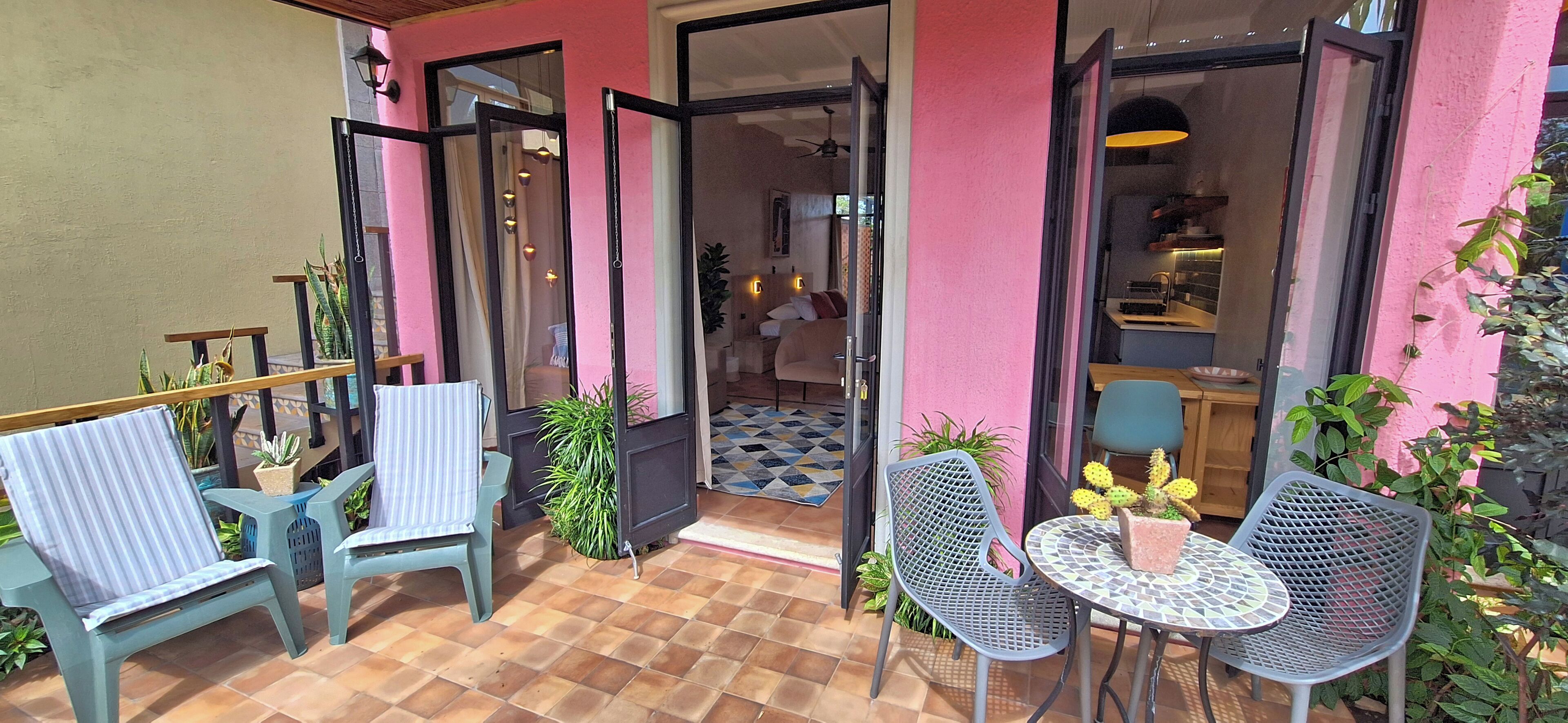An outdoor patio with a checkered floor, two chairs, a small table, and potted plants.