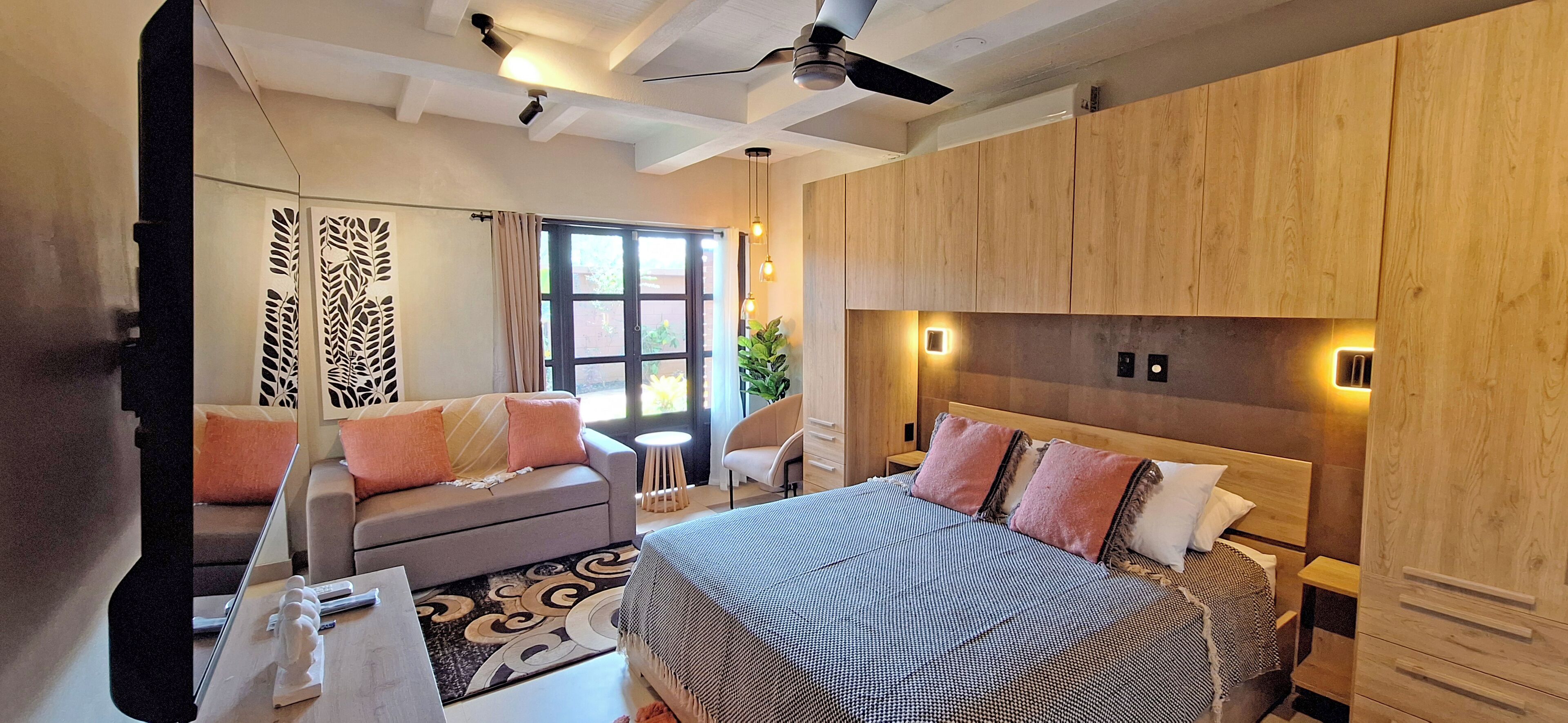A modern hotel room with a large bed, a sofa, a desk, and a ceiling fan.