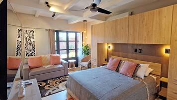 A modern hotel room with a large bed, a sofa, a desk, and a ceiling fan.