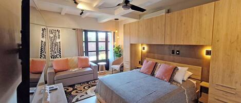 A modern hotel room with a large bed, a sofa, a desk, and a ceiling fan.