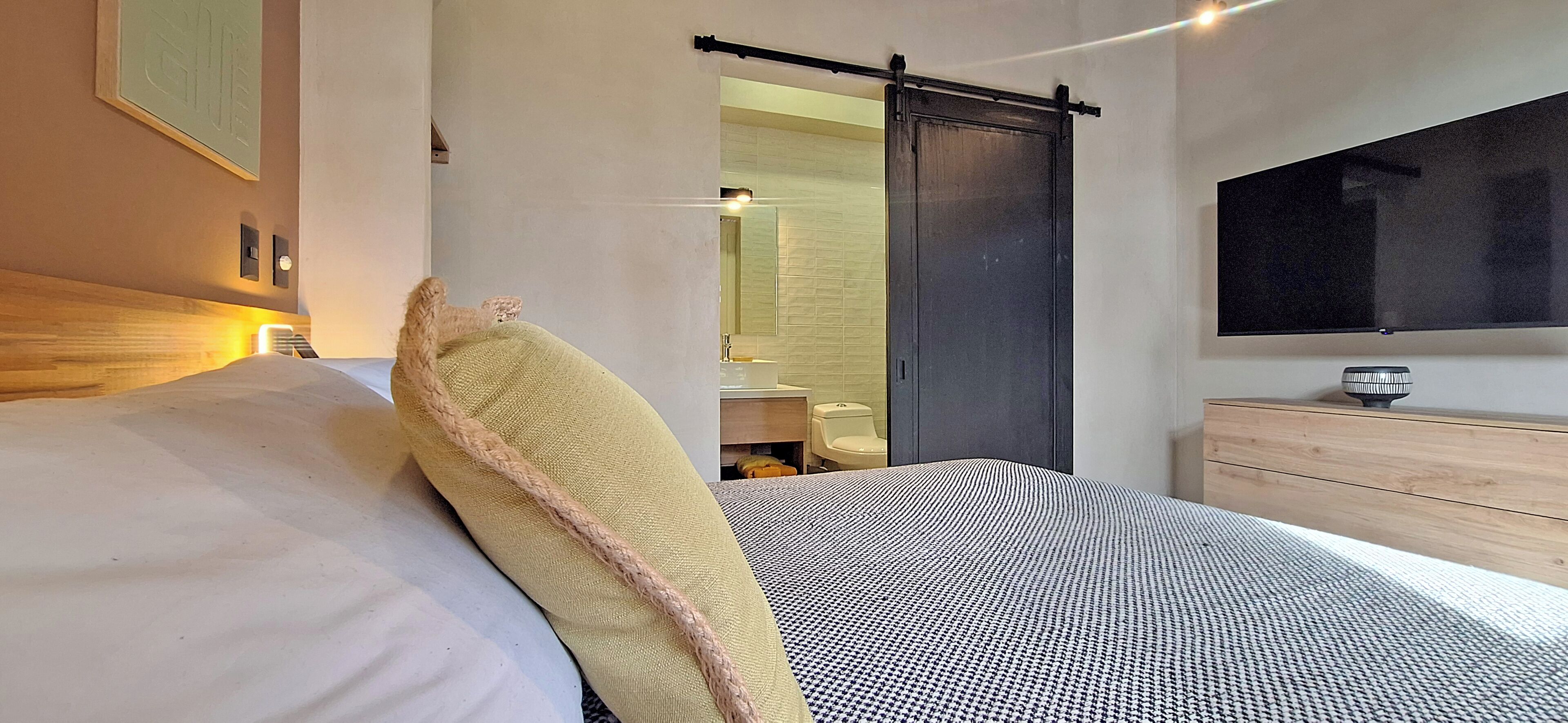 A modern bedroom with a bed, a large mirror, a TV, and a wooden dresser.