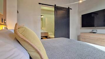 A modern bedroom with a bed, a large mirror, a TV, and a wooden dresser.