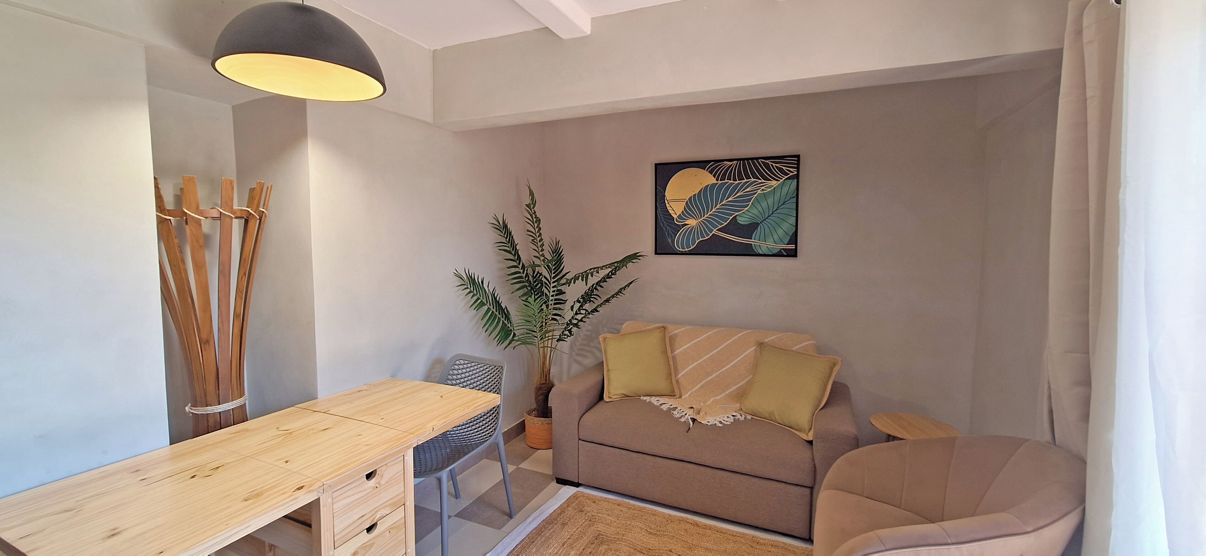 Una sala de estar acogedora con una mesa de madera, un sofá, una planta en maceta y una obra de arte colgada en la pared.