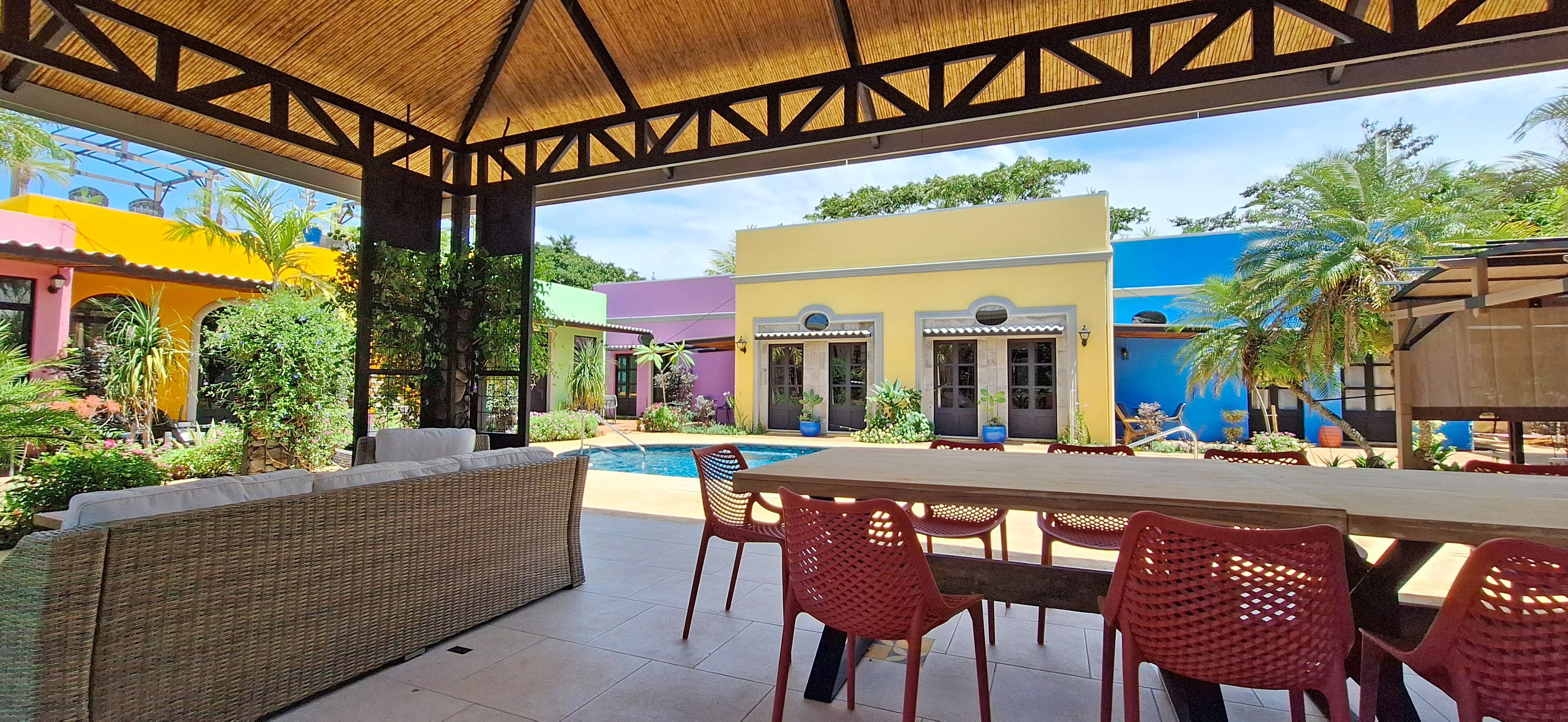An outdoor patio area with a pool, wicker furniture, and red plastic chairs.