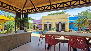 An outdoor patio area with a pool, wicker furniture, and red plastic chairs.
