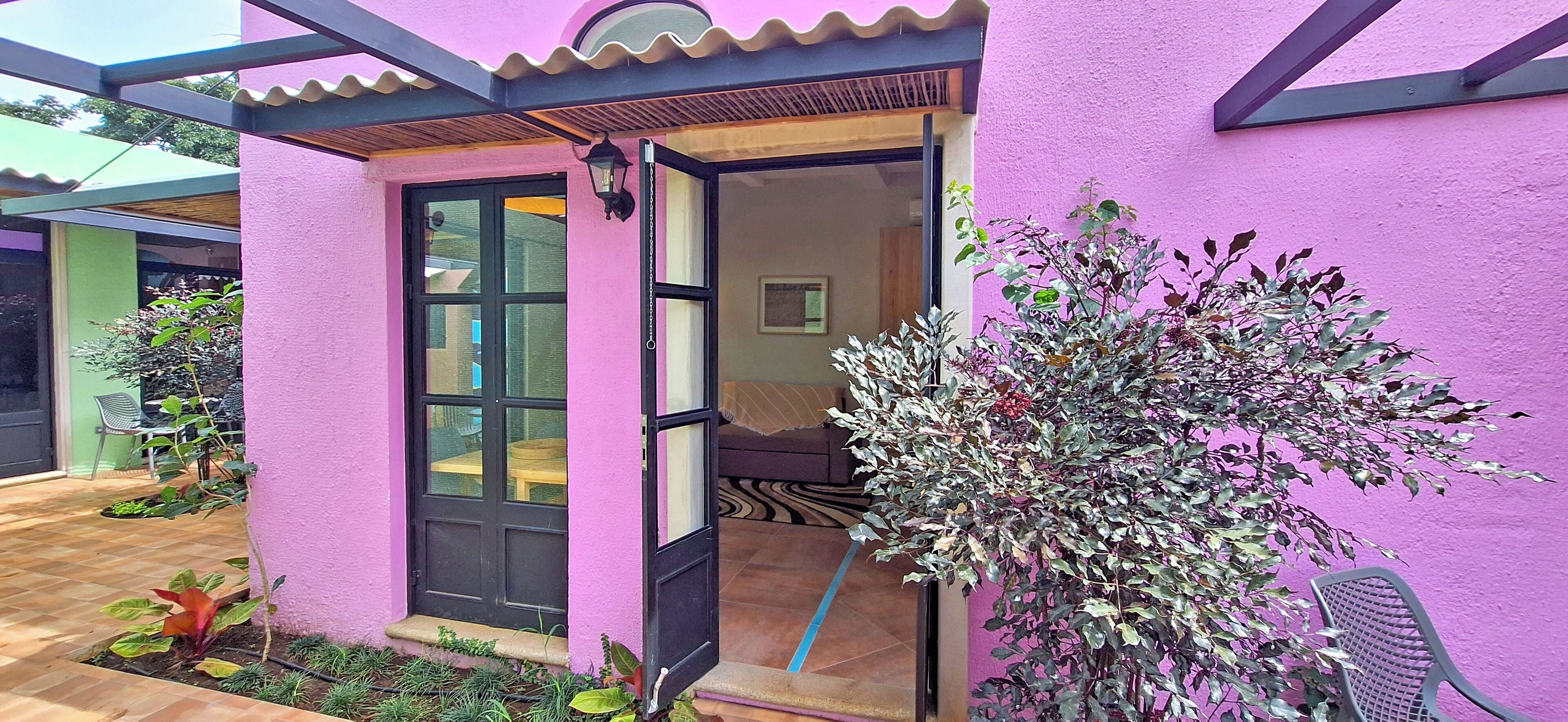 A pink building with a black door and windows, a small porch, and a chair outside.