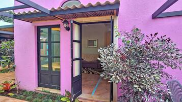 A pink building with a black door and windows, a small porch, and a chair outside.