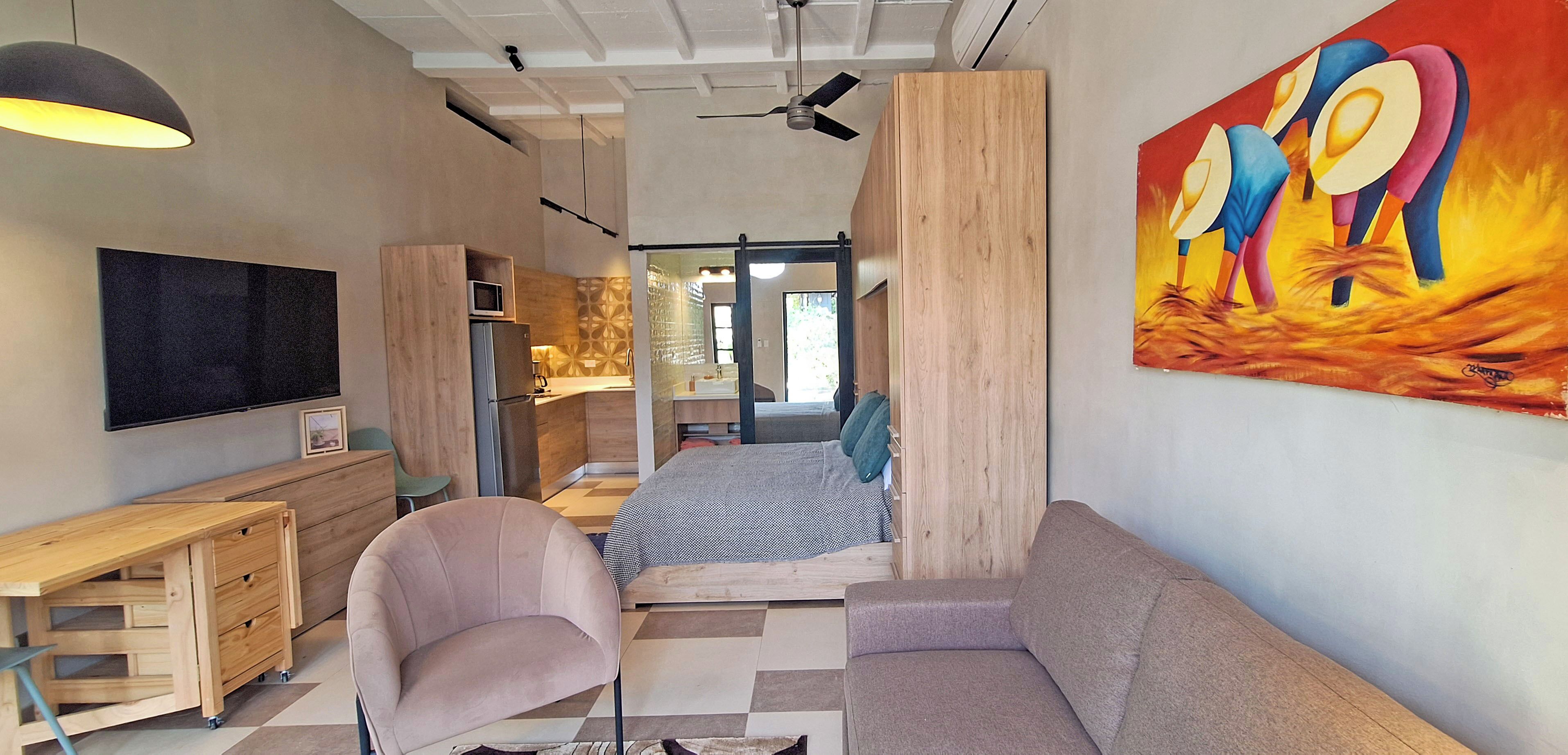 A modern living room with a sofa, armchair, wooden desk, and a flat-screen TV.