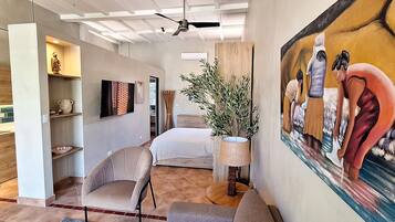 A modern bedroom with a bed, a chair, a painting, and a plant.