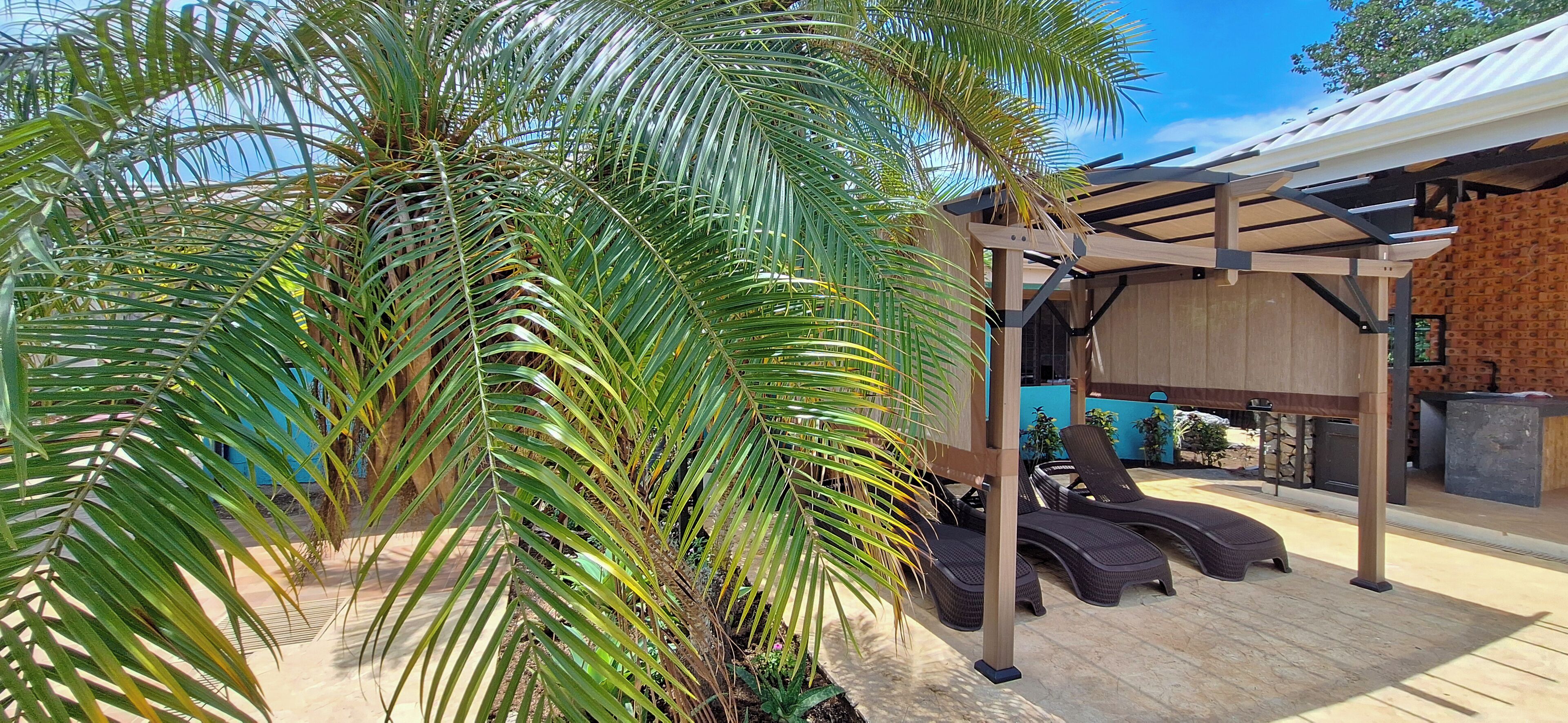 A covered outdoor area with a pergola, lounge chairs, and a stone wall.