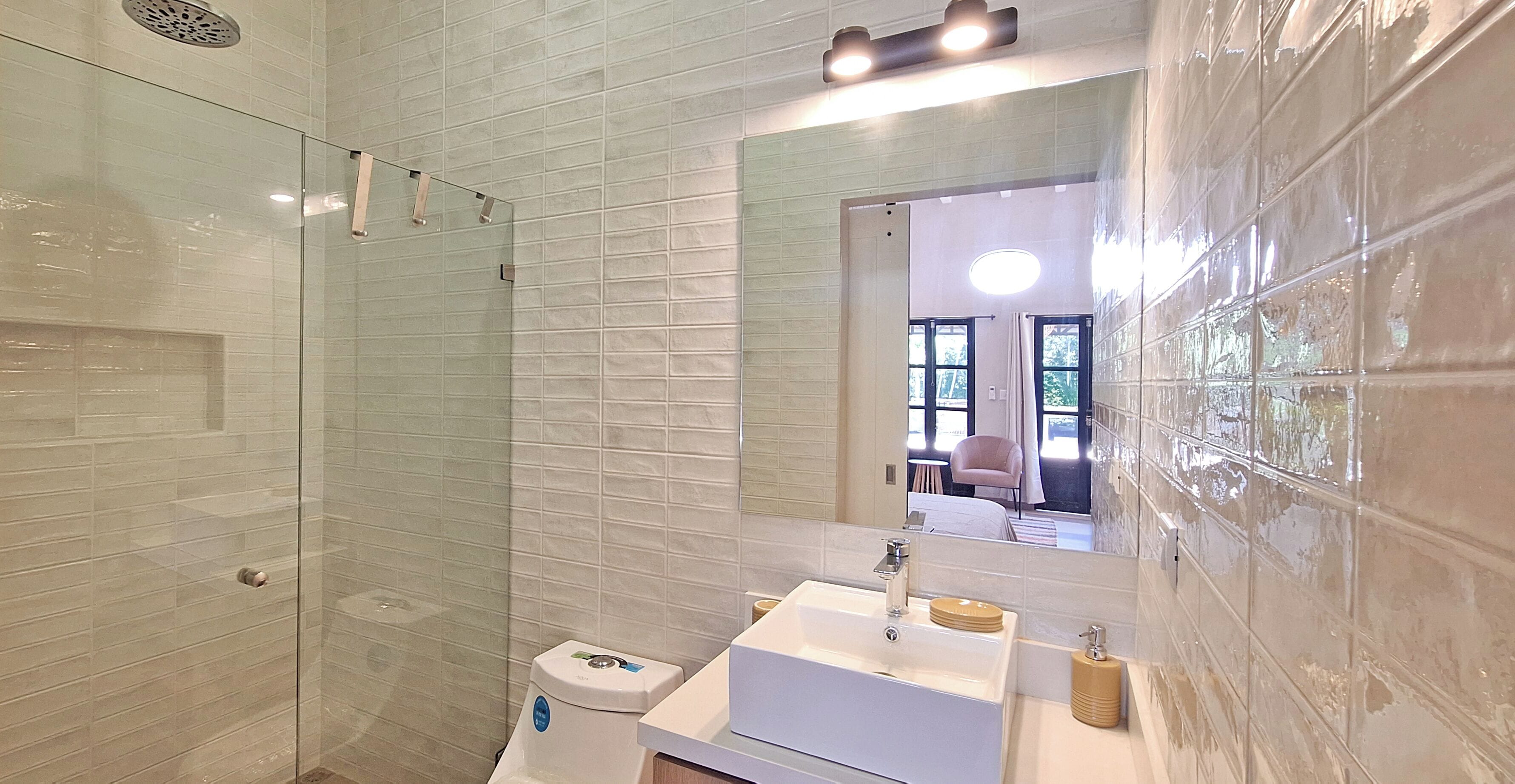 Ein modernes Badezimmer mit Duschkabine, Toilette und Waschbecken mit Spiegel darüber.