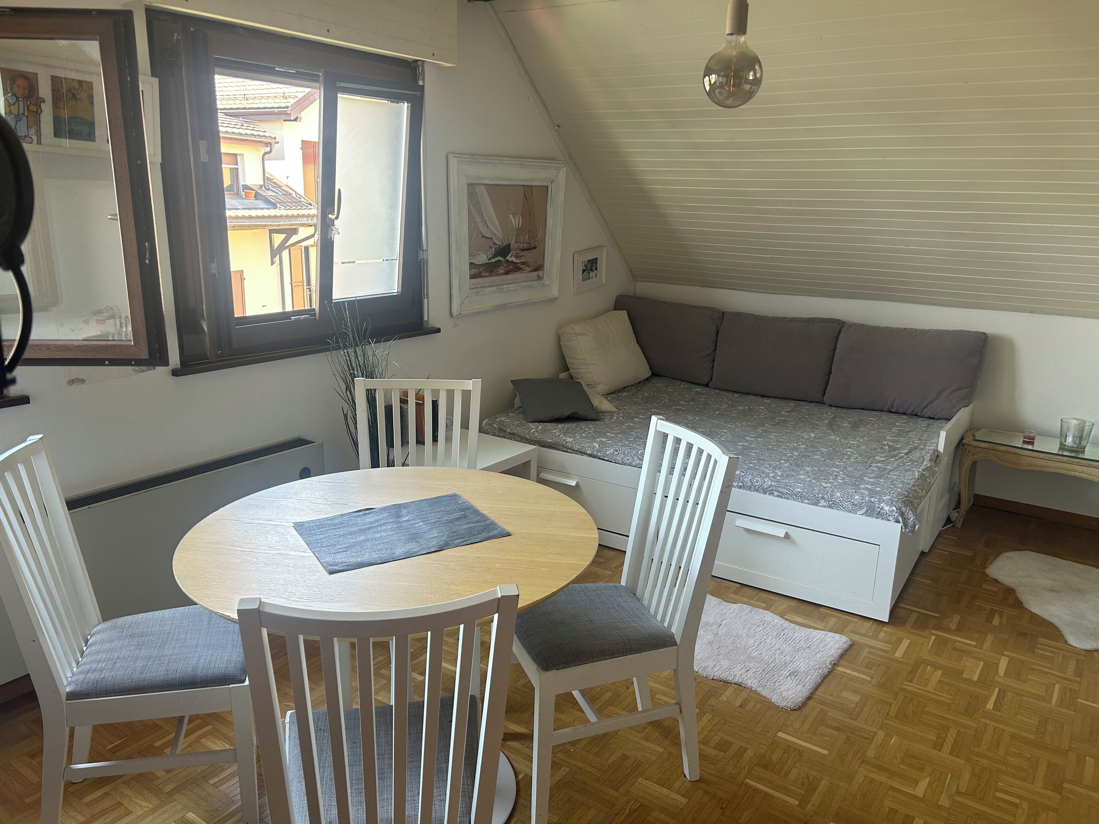 Una stanza accogliente con un tavolo rotondo in legno, due sedie bianche, un divano letto e un piccolo tavolino in vetro.