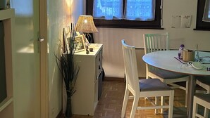 A compact kitchen with a dining area, featuring a wooden herringbone floor, a white table, and chairs. - Cosy studio with views of Lake Geneva and Mont Blanc (Arzier-Le Muids)