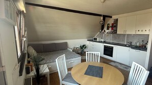 A compact living space with a dining table, chairs, a sofa, and a kitchenette. - Cosy studio with views of Lake Geneva and Mont Blanc (Arzier-Le Muids)