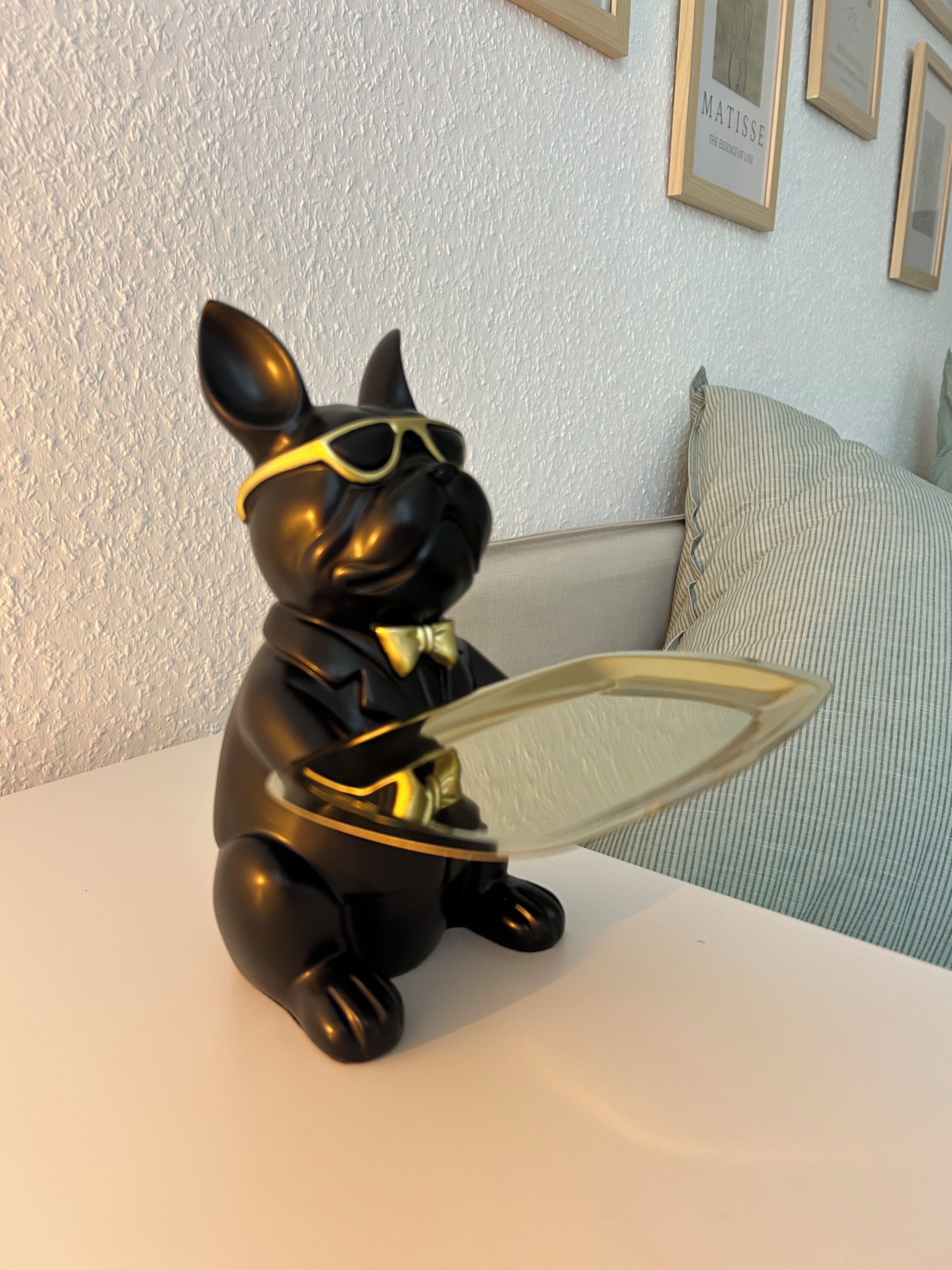 Une figurine de chien noir portant des lunettes de soleil et tenant un miroir, posée sur une surface blanche.