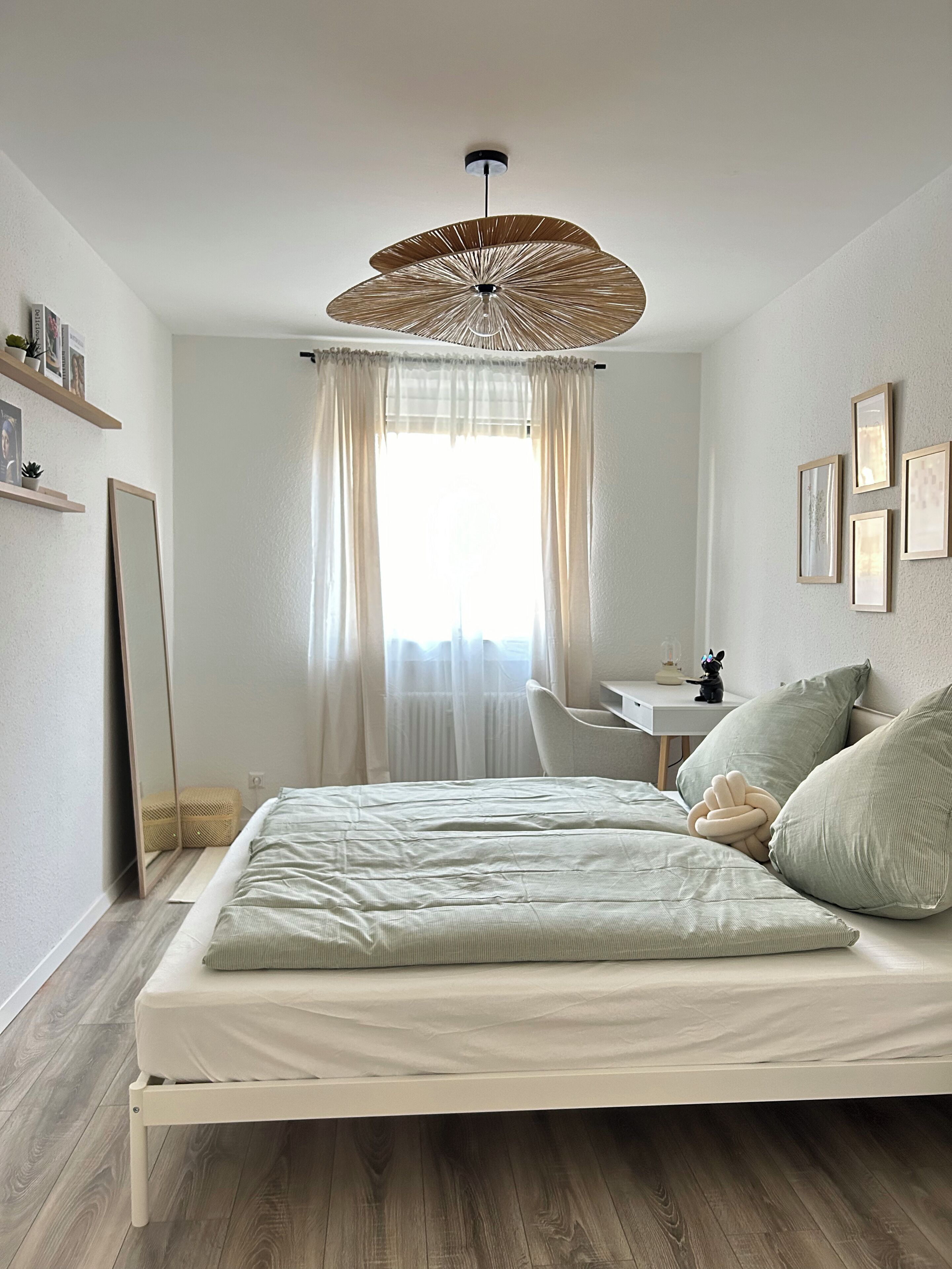 Un dormitorio con cama, escritorio, silla, lámpara colgante y ventana con cortinas.