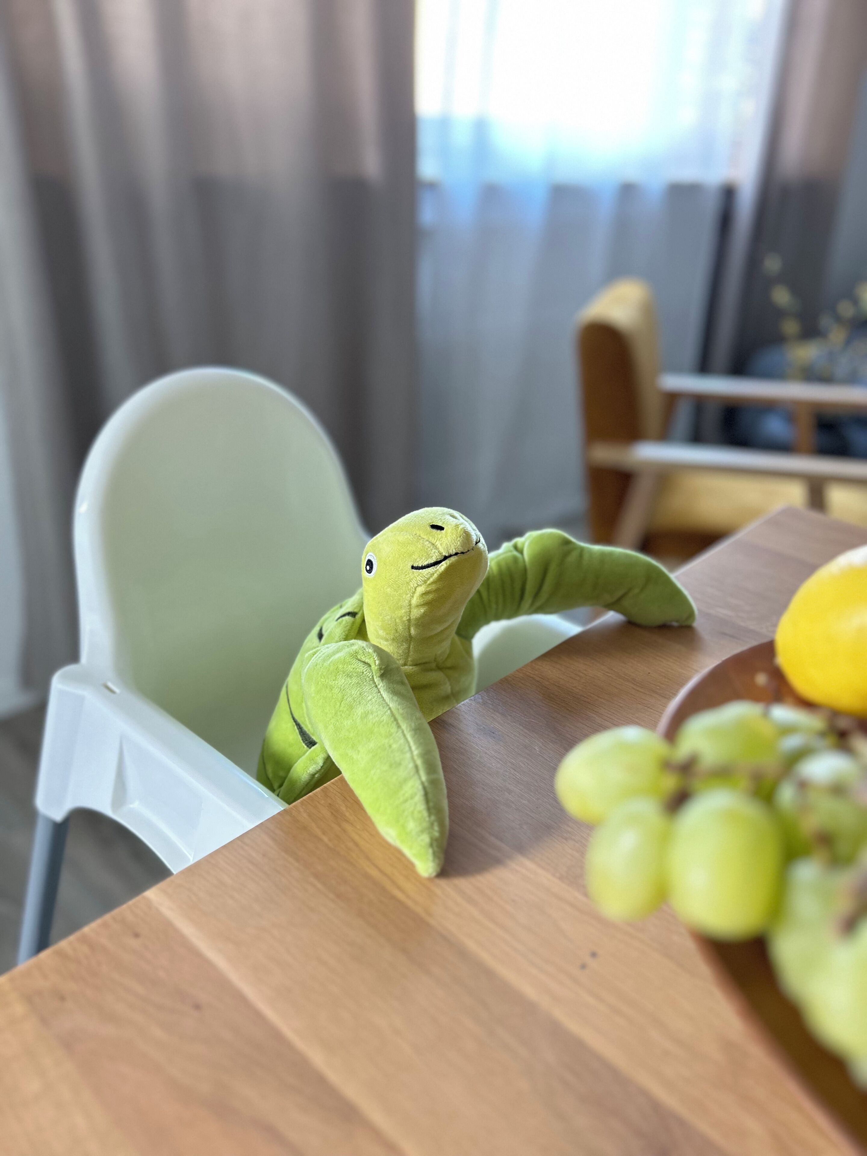 Un ranocchio di peluche verde su un tavolo di legno con una ciotola di uva verde.