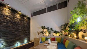 Een modern interieur met een stenen muur, een houten tafel en een kleurrijke bank, plus verschillende planten.