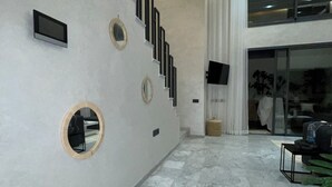Een modern interieur met een marmeren vloer, een trap met ronde spiegels, en een groot raam met gordijnen.