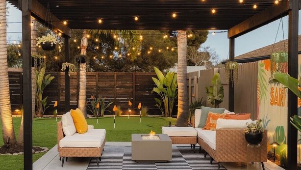 An outdoor patio with a wooden pergola, string lights, a fire pit, and outdoor furniture.