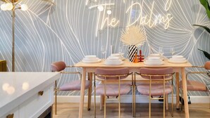 A dining area with a table set for four, a neon sign reading "Meet me by The Dalm," and a decorative plant.