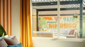 A room with a view of a colorful wall mural reading "Greetings from SAN DIEGO" and a wicker sofa with cushions.