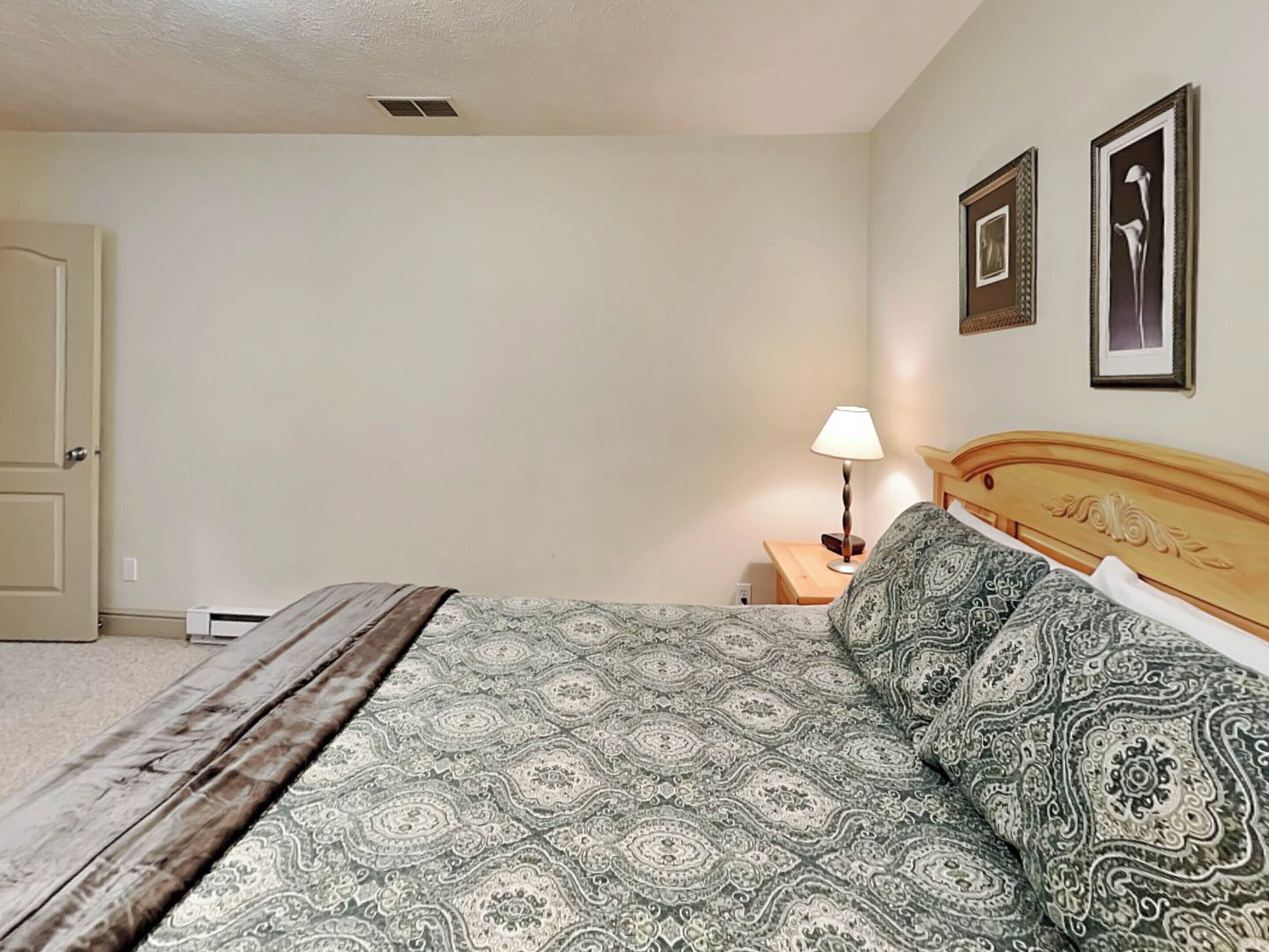 A bedroom with a bed, a nightstand, a lamp, and two framed pictures on the wall.
