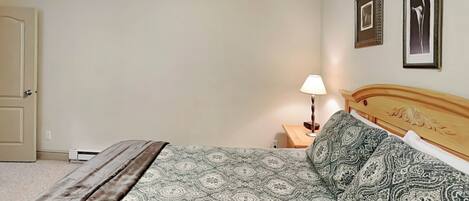 A bedroom with a bed, a nightstand, a lamp, and two framed pictures on the wall.