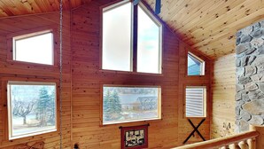 A cabin with wooden walls, large windows, a stone wall, and a wooden railing. - Cedar Shores Villa 10 by Taylor Made Deep Creek (McHenry)