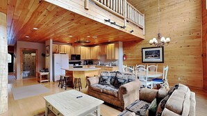 A spacious living area with a wooden ceiling, a dining table, a sofa, and a kitchen in the background. - Cedar Shores Villa 10 by Taylor Made Deep Creek (McHenry)
