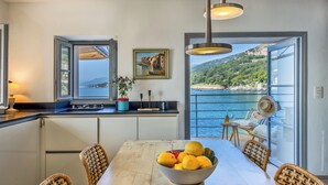 A kitchen with a view of the sea, a dining table with fruit, and wicker chairs. - Maison de pêcheur dans le Cap Corse (Erbalunga)