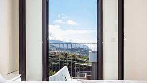 Une chambre avec un grand lit, une vue sur un paysage montagneux depuis un balcon et un mur blanc.