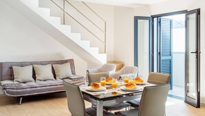 Un salon moderne avec un canapé, une table à manger et des chaises. On aperçoit un escalier au fond.