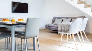 Un salon moderne avec une table à manger dressée pour le petit-déjeuner, un canapé et un escalier.