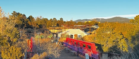 Un sendero que lleva a una estructura tipo tienda blanca con toldo rojo, rodeada de árboles otoñales y plantas en macetas.