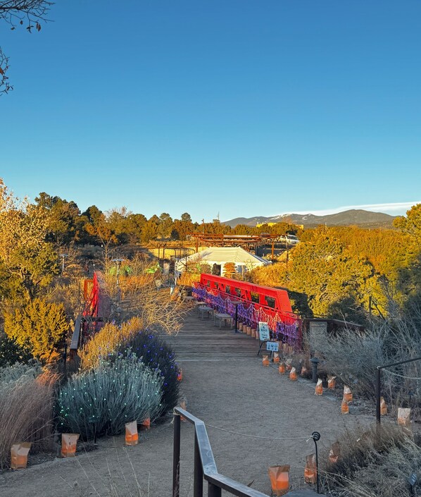 A pathway leading to a white tent structure with a red canopy, surrounded by autumnal trees and potted plants.