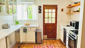 A compact kitchen with white cabinets, a microwave, and a stove. There is a patterned rug on the floor and a window with curtains. - Rustic charm meets comfort—king bed, AC, patio, walk 5 mins Canyon Rd, and Plaza (Santa Fe)