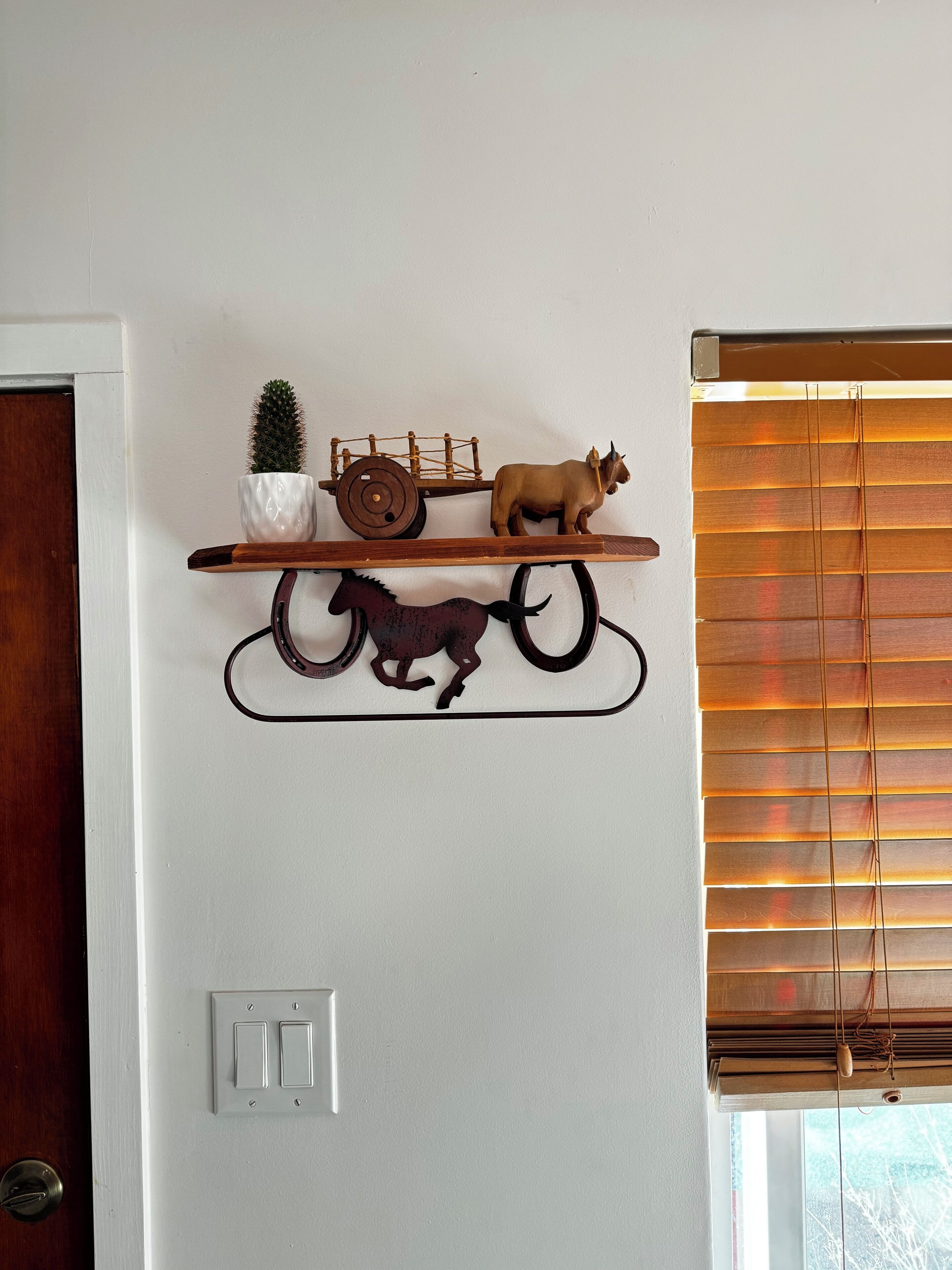 A wall-mounted shelf with a cactus, a wooden cart, and a horse figurine.