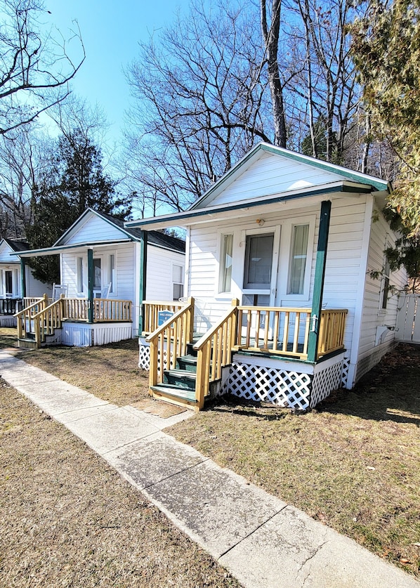 A row of small, single-story cabins with wooden railings and steps leading to the front door. - Dollhouse #4 at Portage Point Resort (Onekama)