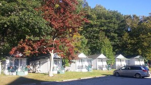 A row of white cabins with green railings, a tree with red leaves, and a parked car in front. - Dollhouse #4 at Portage Point Resort (Onekama)