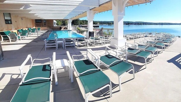 A poolside area with lounge chairs and a pool under a wooden canopy. - Dollhouse #4 at Portage Point Resort (Onekama)