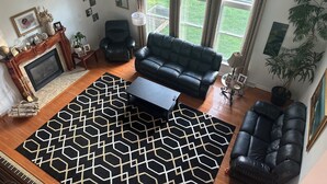 Ein Wohnzimmer mit Kamin, einer schwarzen Ledersofa, einem gemusterten Teppich und Blick ins Freie.